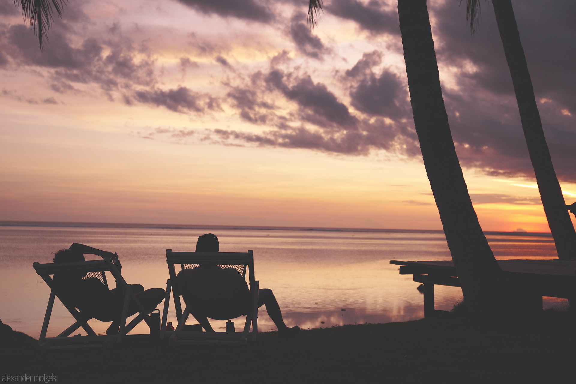 Foto von Silhouetted loungers beneath palms as the sun sets over the calm lagoon in Komave, Fiji.