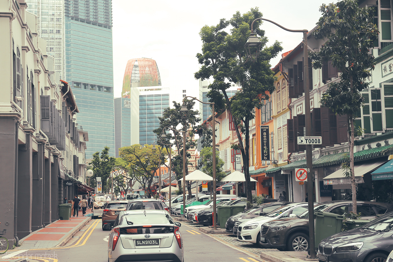 Foto von A charming street in Singapore's Kampong Glam, where heritage shophouses meet modern skyscrapers under a tropical urban canopy.