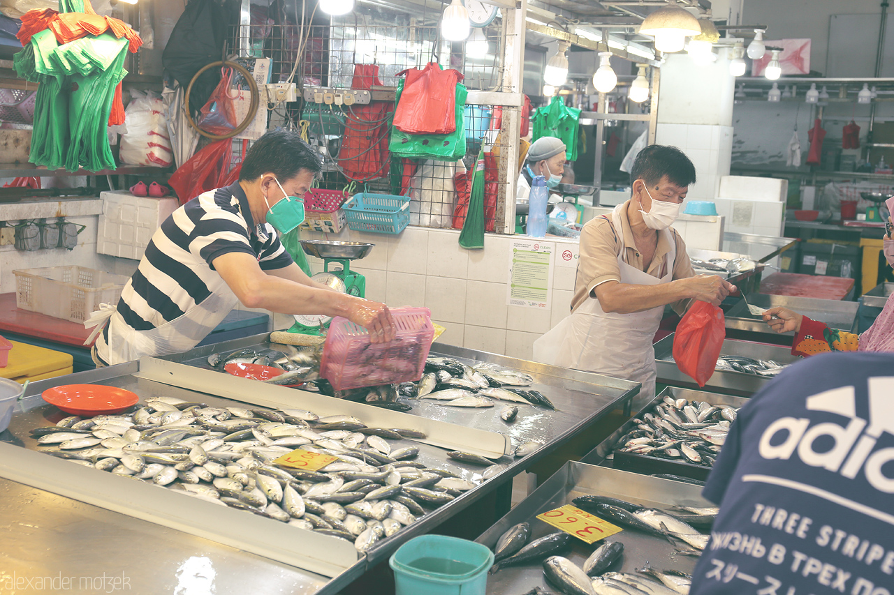 Foto von At a bustling Singapore market, vendors prepare fresh fish, surrounded by colorful bags and produce. A snapshot of local daily life.