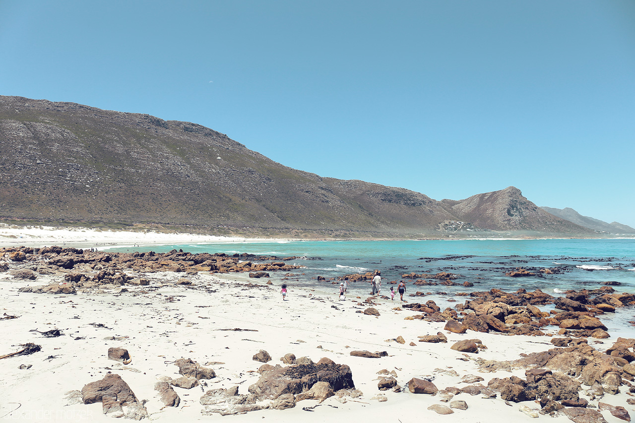 Foto von Explore Cape Town's rugged coastline where the mountains meet the turquoise sea, dotted with boulders and kissed by the clear, sunny skies.