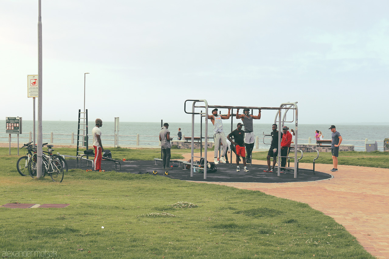 Foto von Locals enjoying a workout at an outdoor gym along Sea Point Promenade, Cape Town, with the Atlantic Ocean as a backdrop.