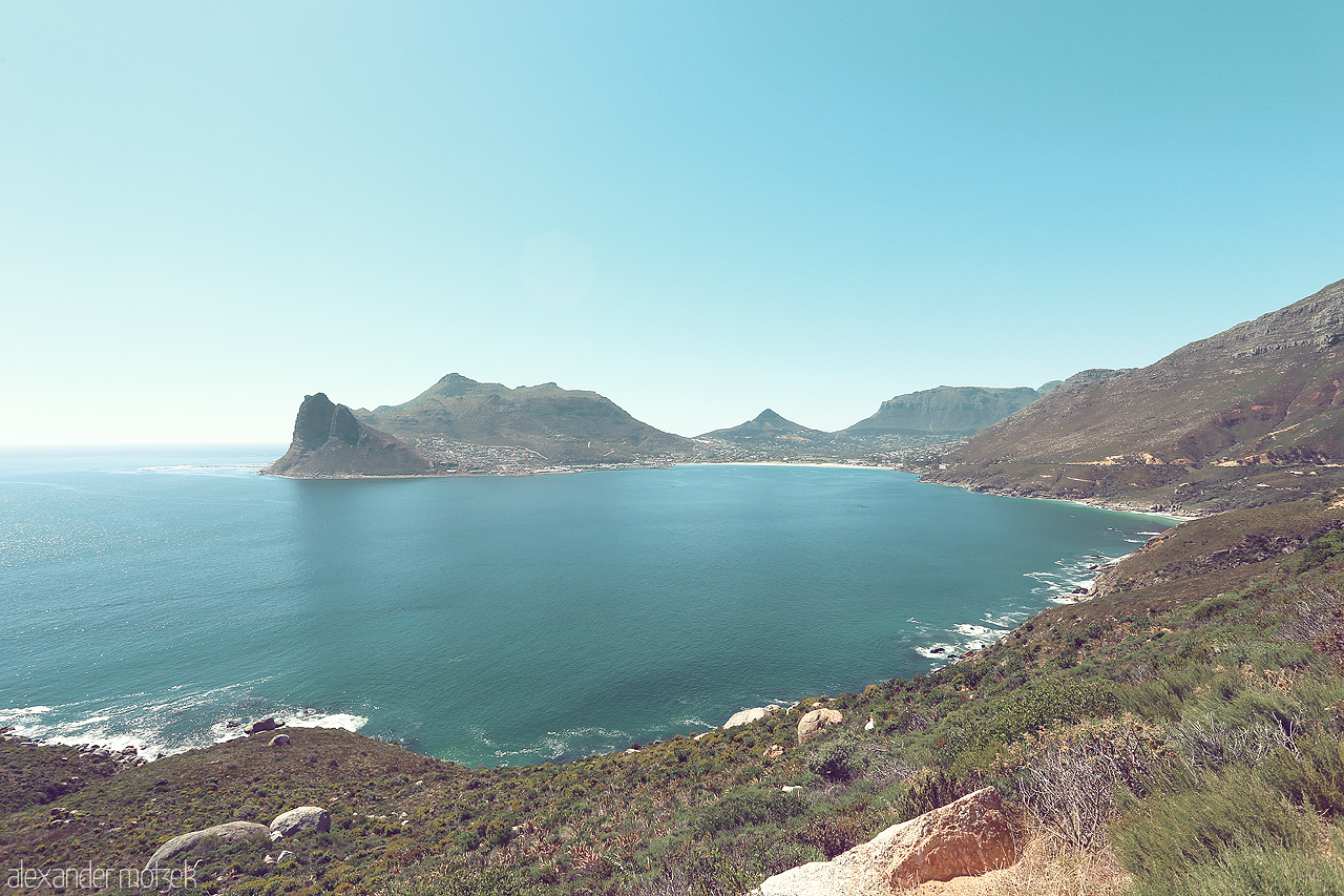 Foto von Majestic view of Hout Bay, Cape Town. Calm azure waters framed by rugged mountains under a clear sky. A tranquil escape on the Western Cape.