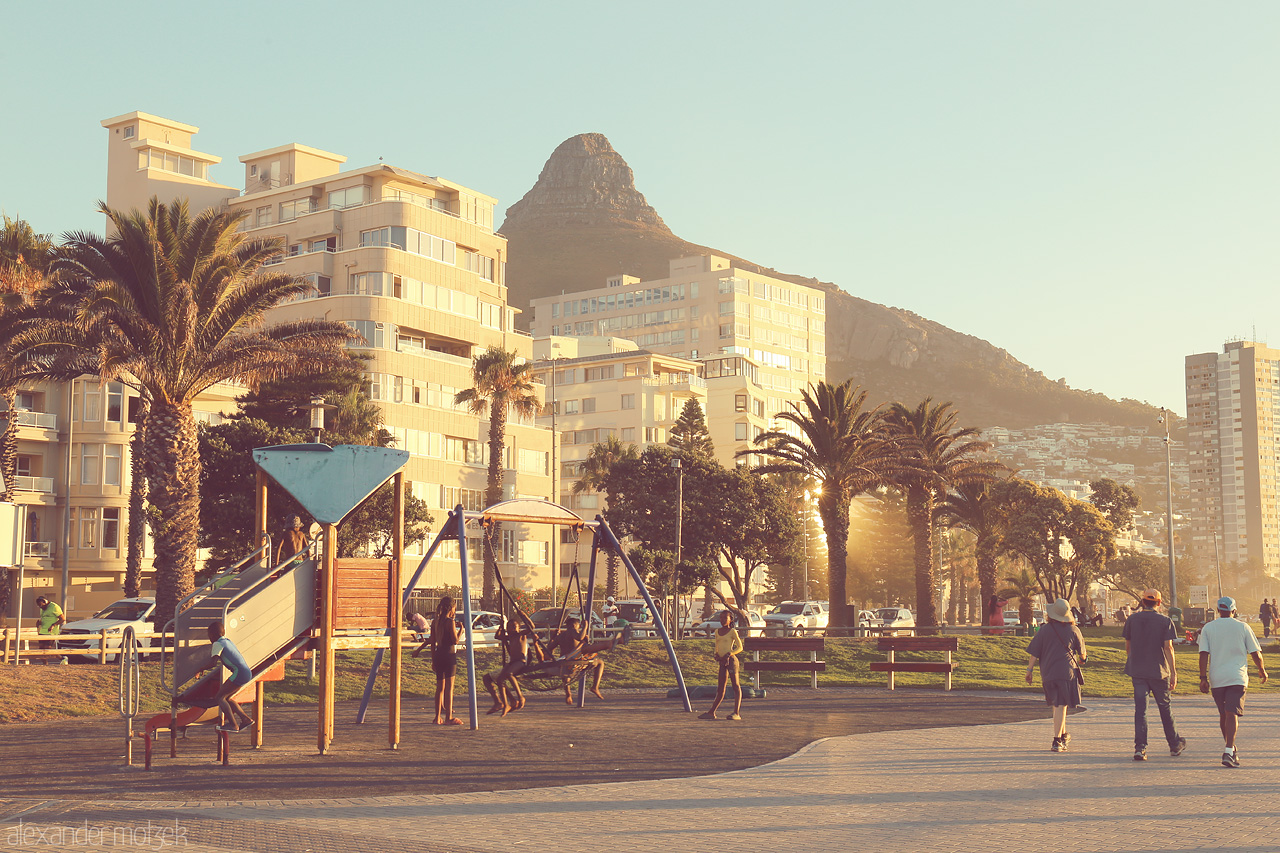 Foto von Sunset glow on Cape Town's coastline with Lion's Head watching over and playful swings bringing joy to the promenade.