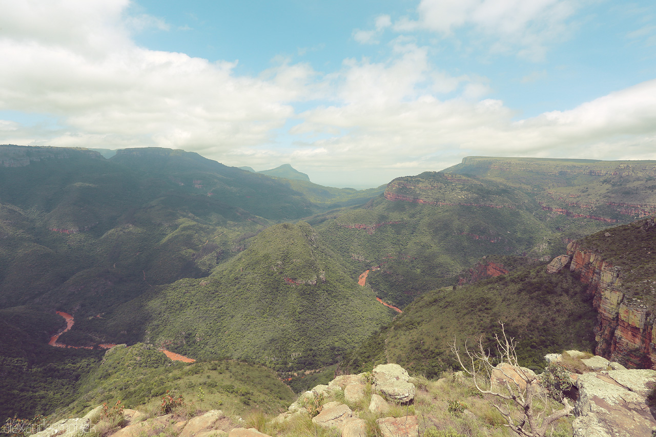 Foto von The vast landscape of Blyde River Canyon, South Africa, unfolds with lush greenery and winding paths beneath a clear blue sky.