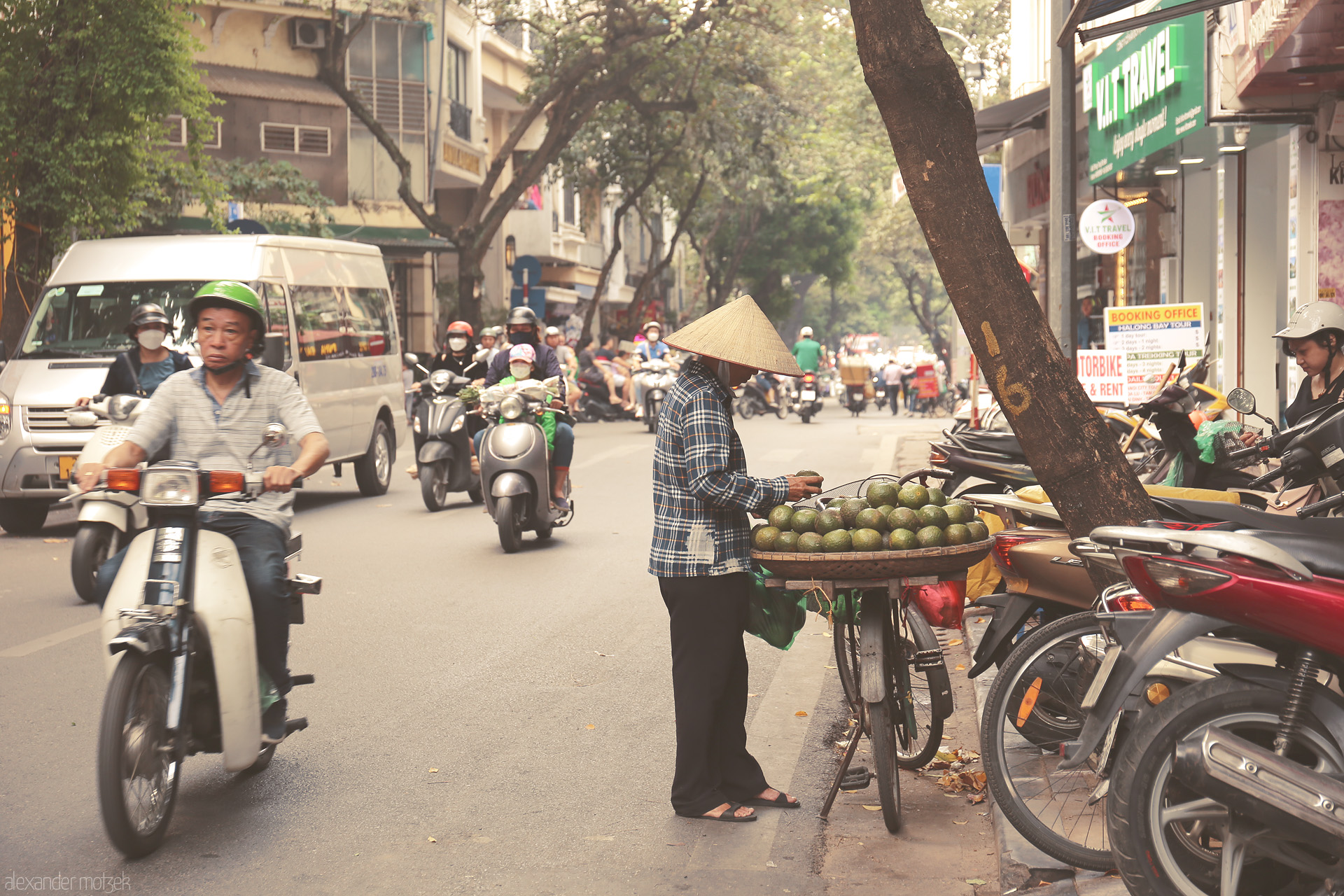 Foto von Street vendor with conical hat and bicycle of avocados amid the lively, scooter-filled Phuong Hàng Bac, Hanoi.