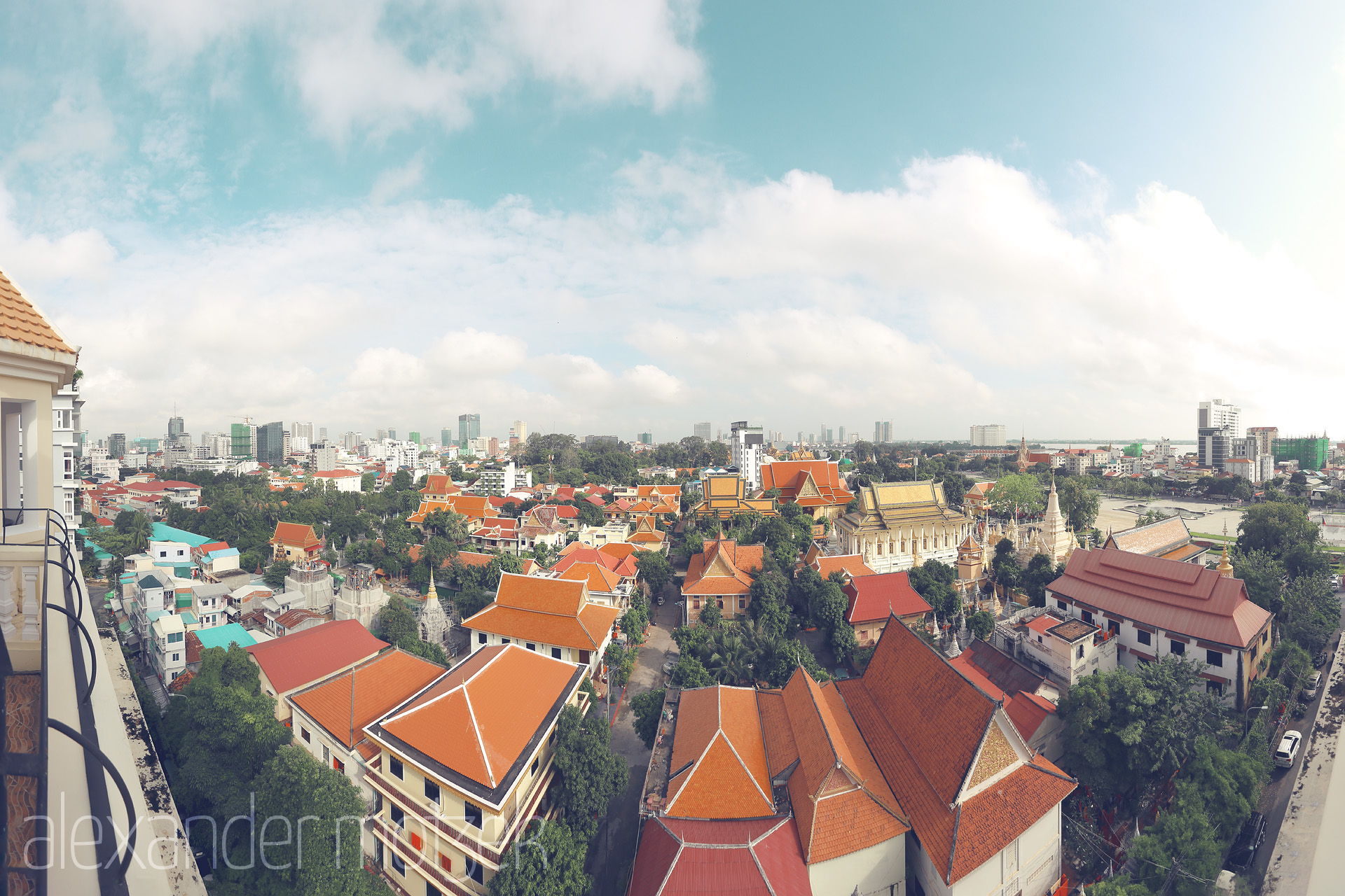 Foto von Sunlit view over Phnom Penh: golden-roofed temples, vibrant red tiles, cityscape, and Mekong River under a dreamy Cambodian sky.