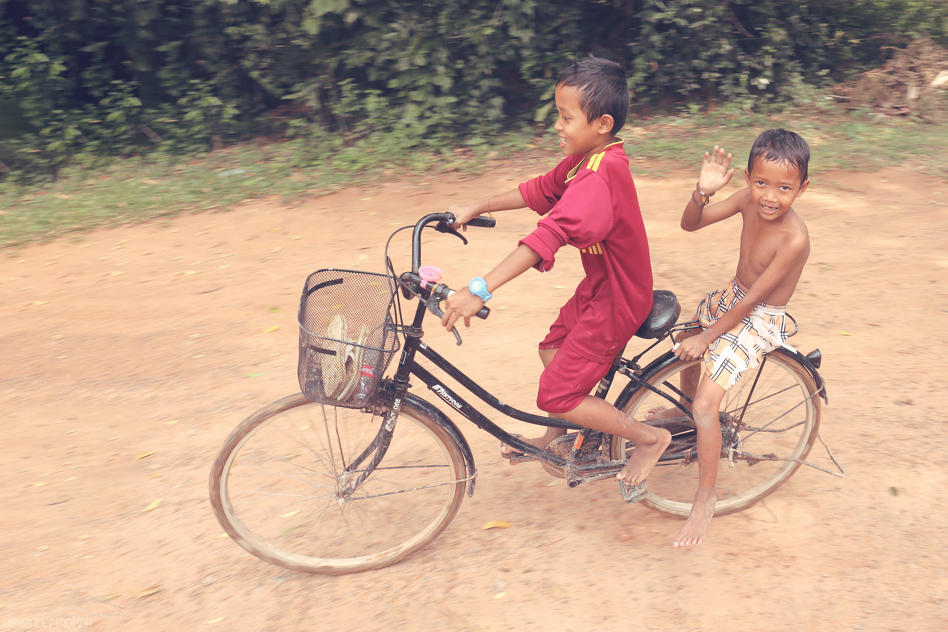 Foto von Two Khmer boys on a bicycle, grinning and carefree, ride a dusty path near Angkor Wat, Siem Reap, capturing the spirit of Cambodian youth.